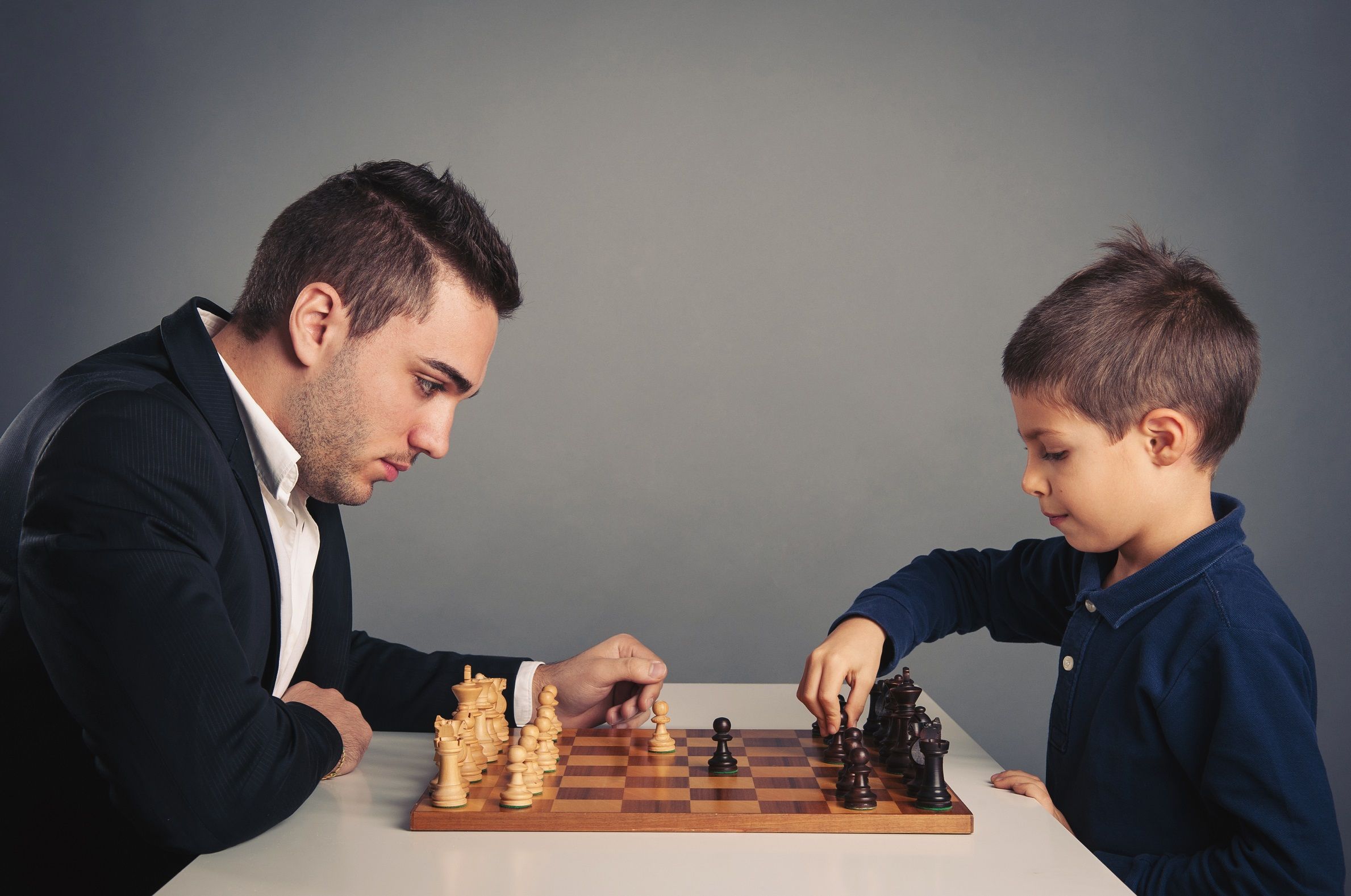 A man in a suit playing chess with a smartly-dressed child.