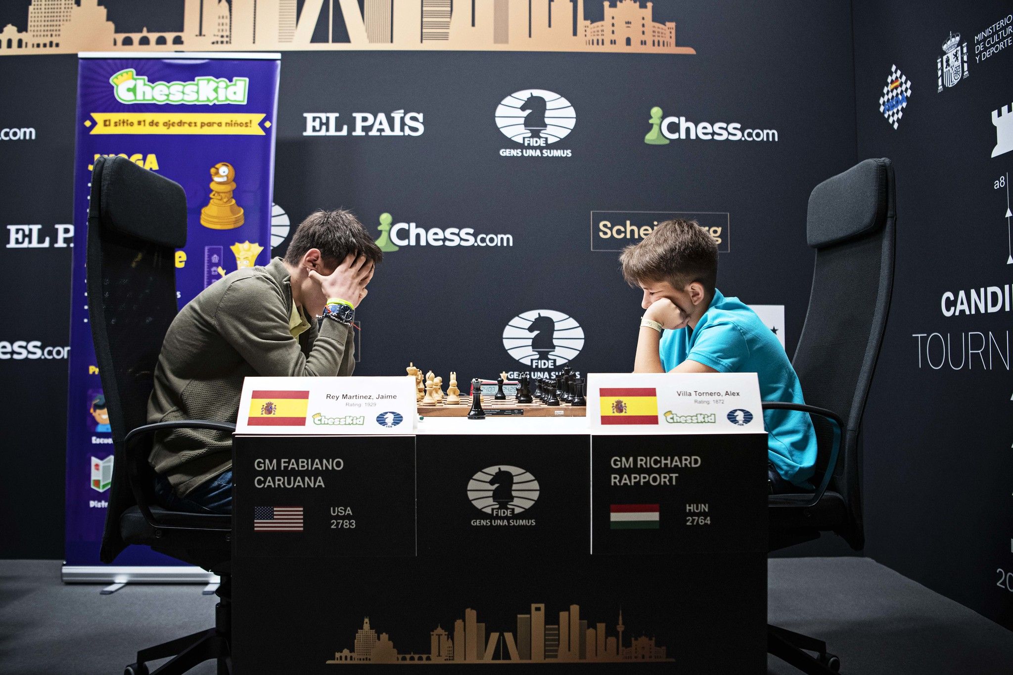 Two young chess players sitting at the official boards for the 2022 Candidates tournament, deep in thought.